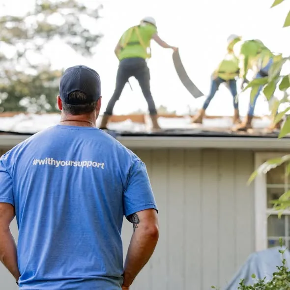 A crew in safety harnesses tearing off an old roof while a supervisor watches.